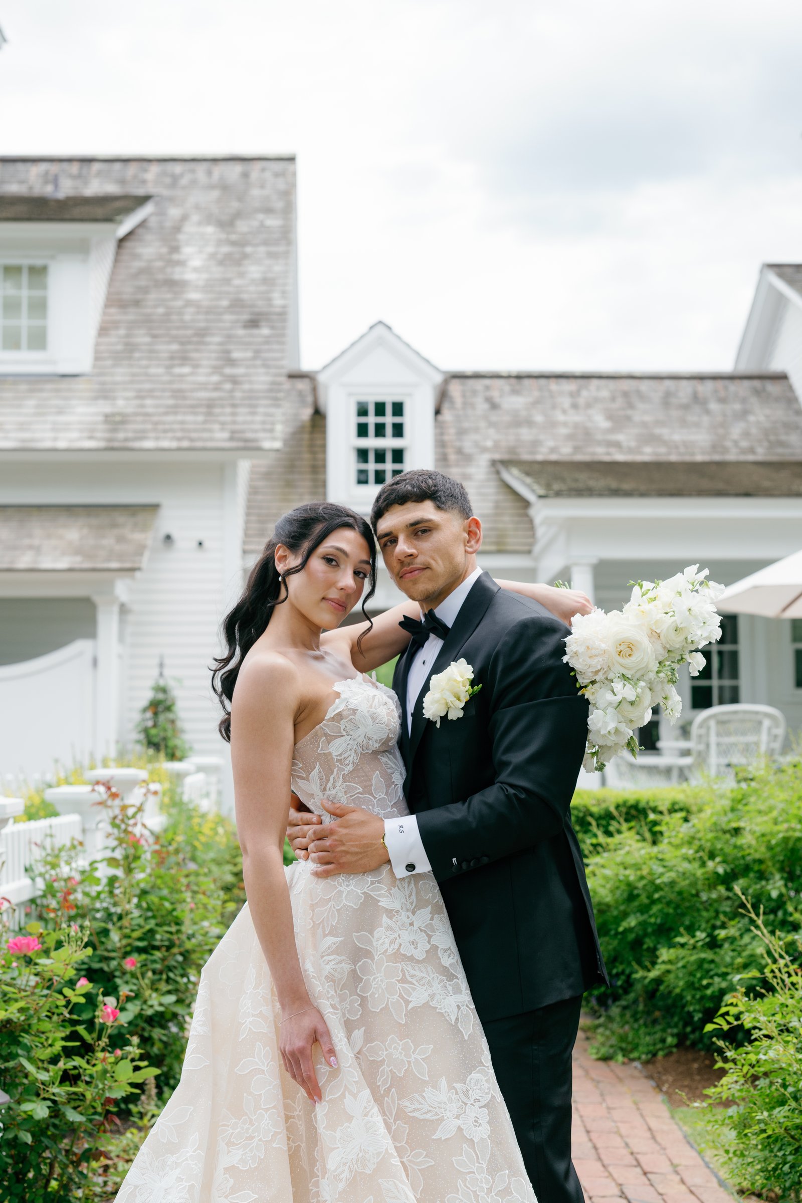 Kayla and Avery arm in arm on the garden path in front of the white house at Smith Farm Gardens
