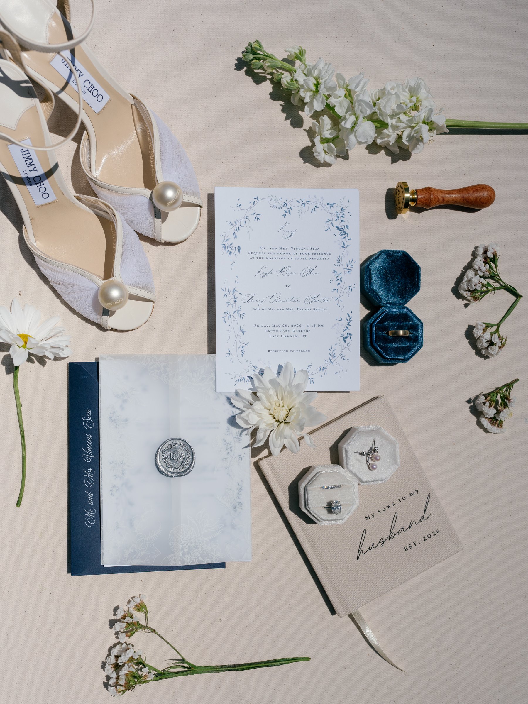 Kayla's shoes, invitation suite, ring boxes and vow book laid out with white flowers