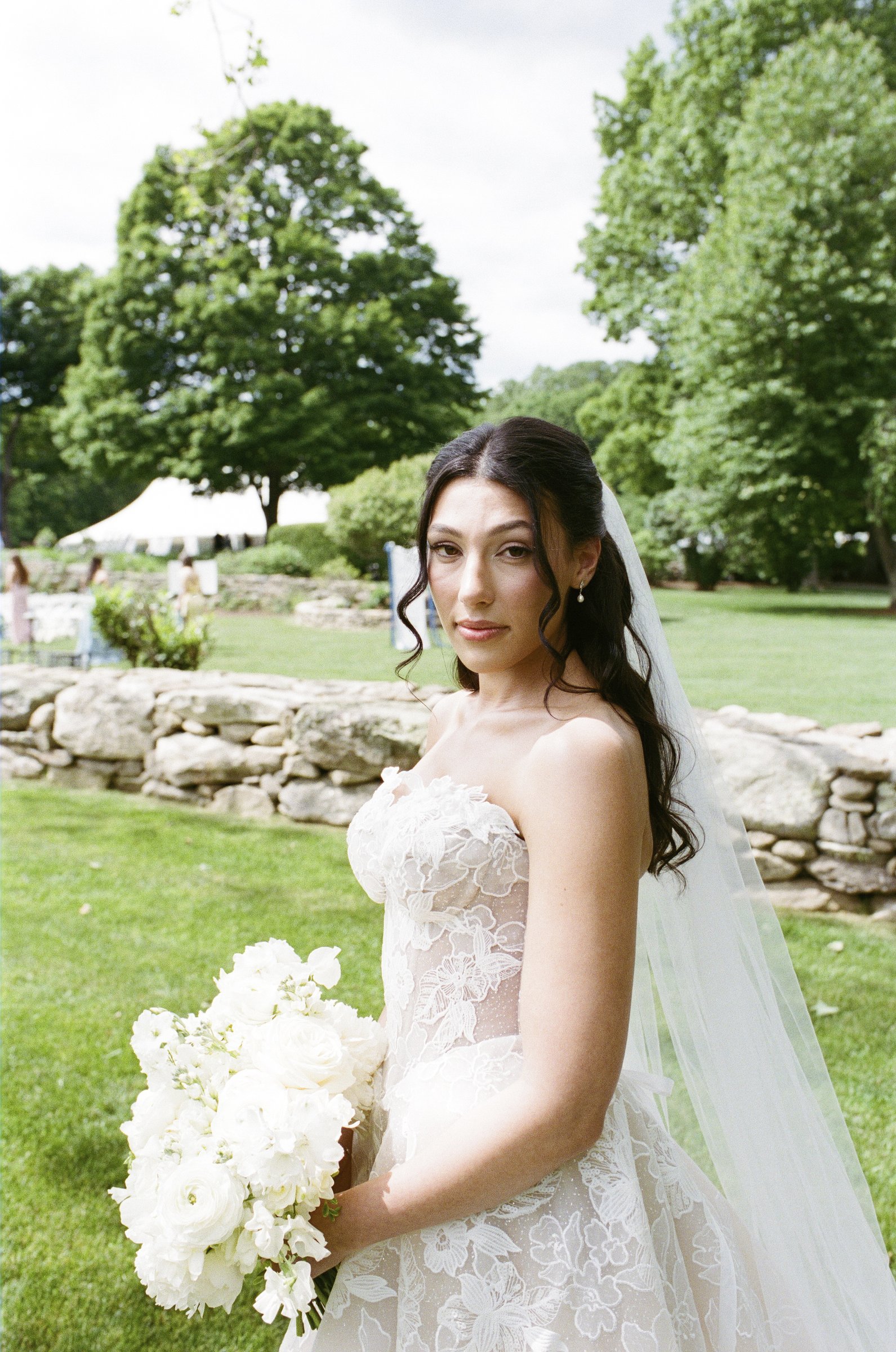 Kayla with her veil and bouquet by the stone wall