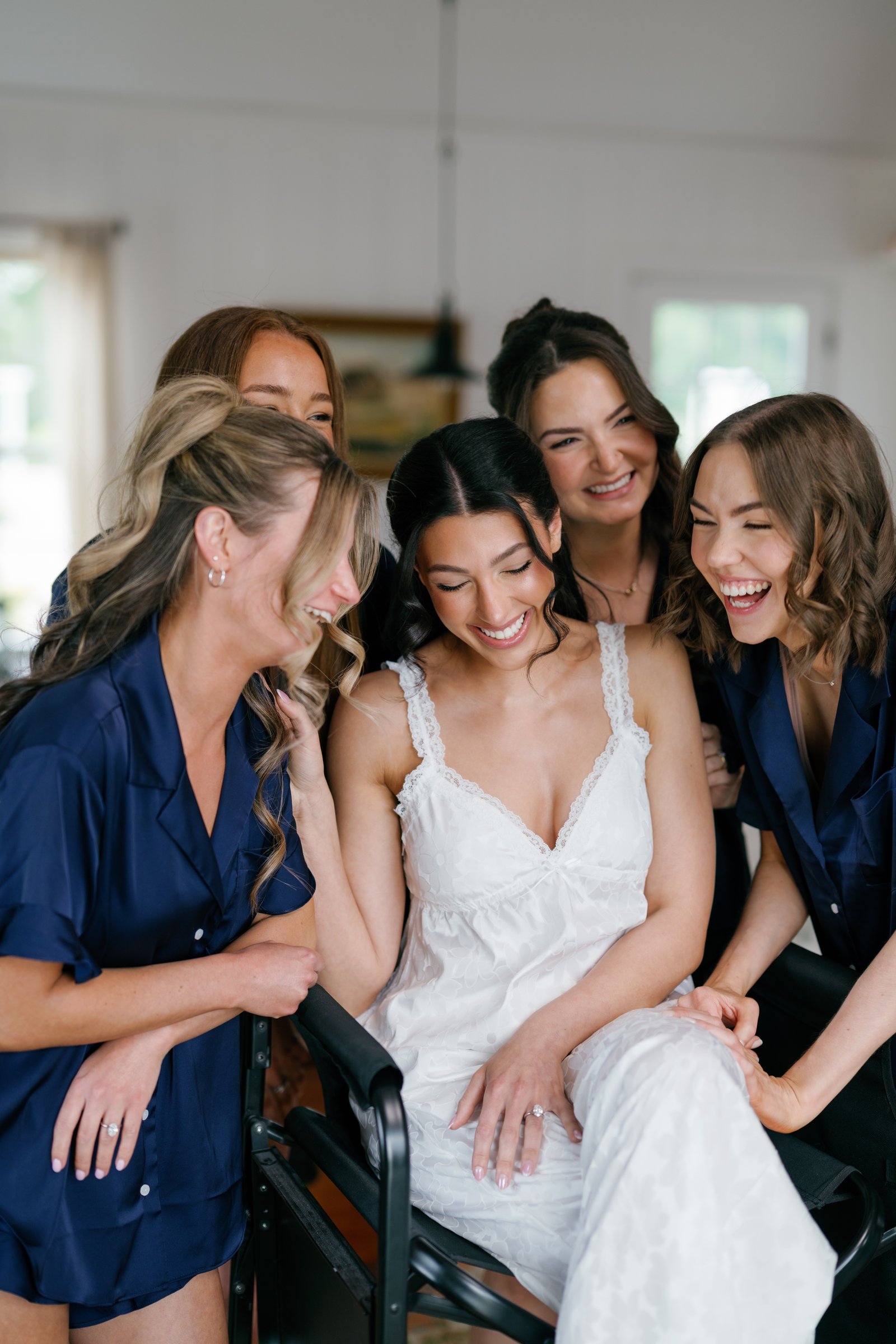 Kayla and her bridesmaids in navy robes laughing together in the bridal cottage