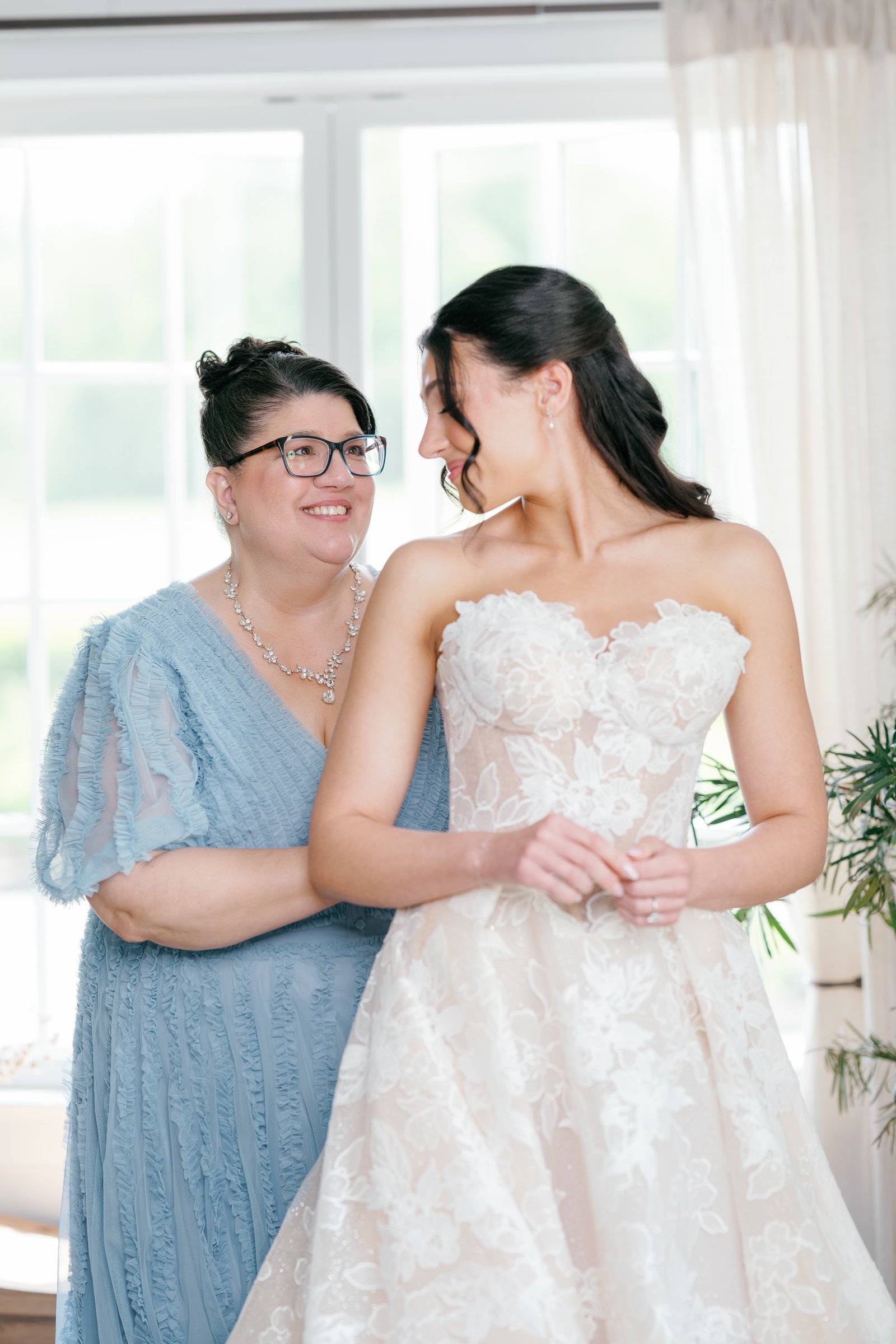 Kayla and her mother, in a blue dress, smiling at each other by the window