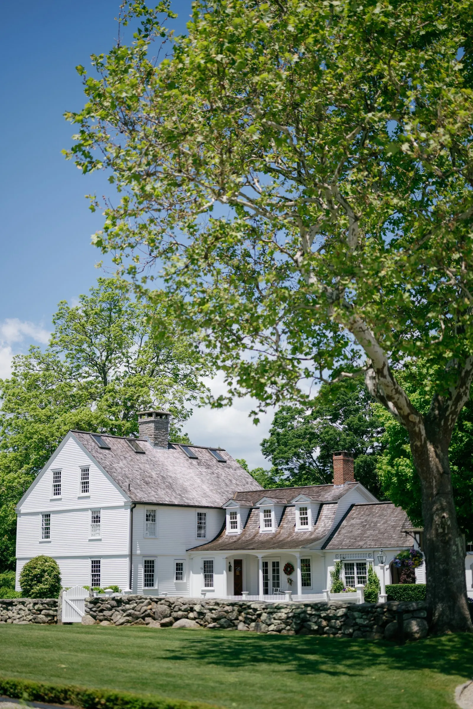 The white farmhouse at Smith Farm Gardens under a sycamore on a blue-sky day