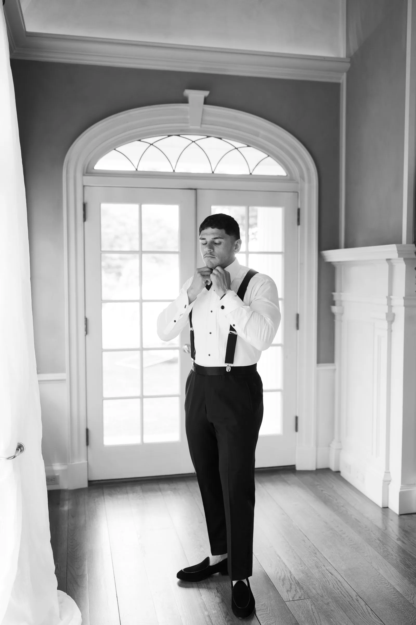 Avery fastening his cuffs by the arched doorway, in black and white