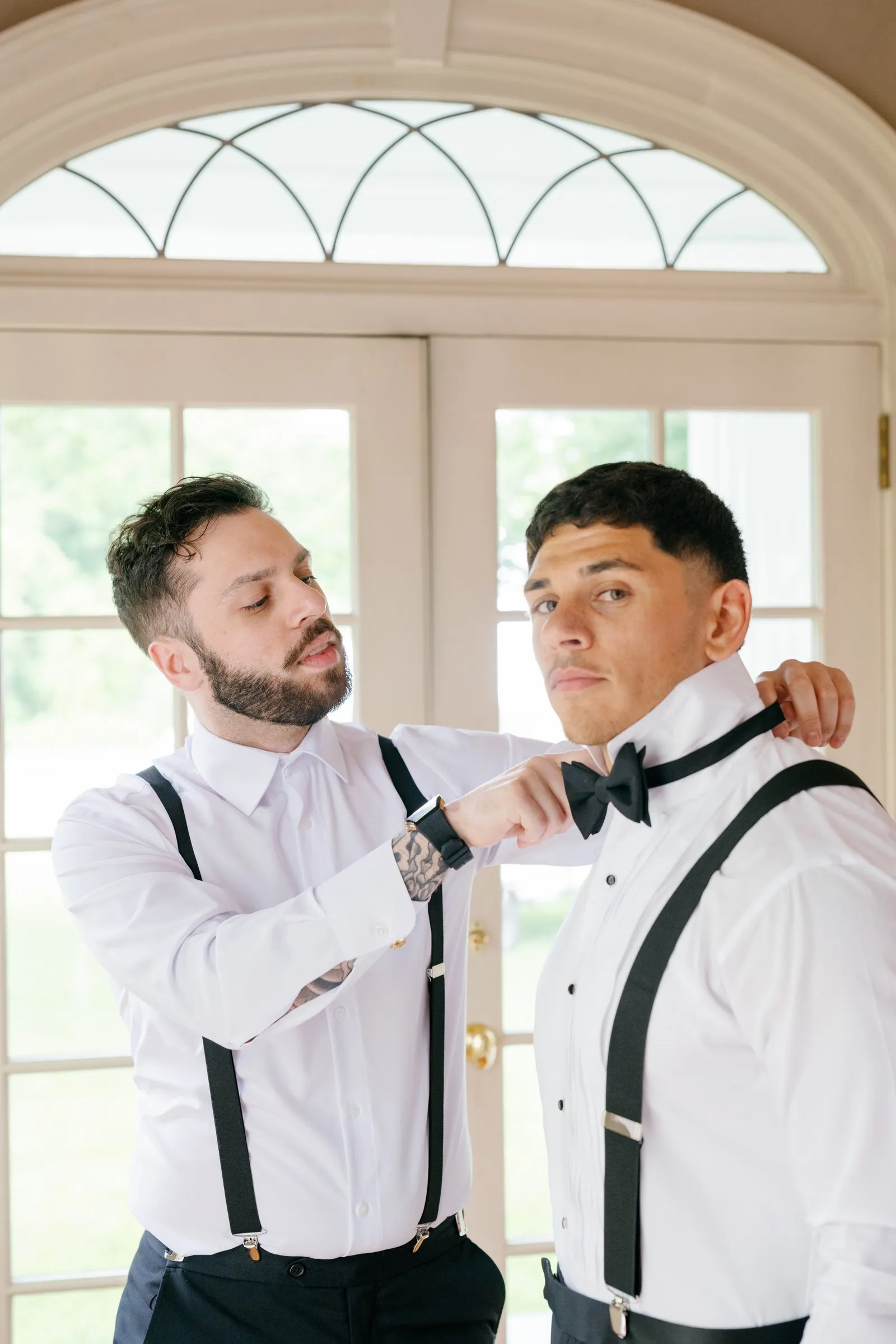 A groomsman helping Avery with his bow tie