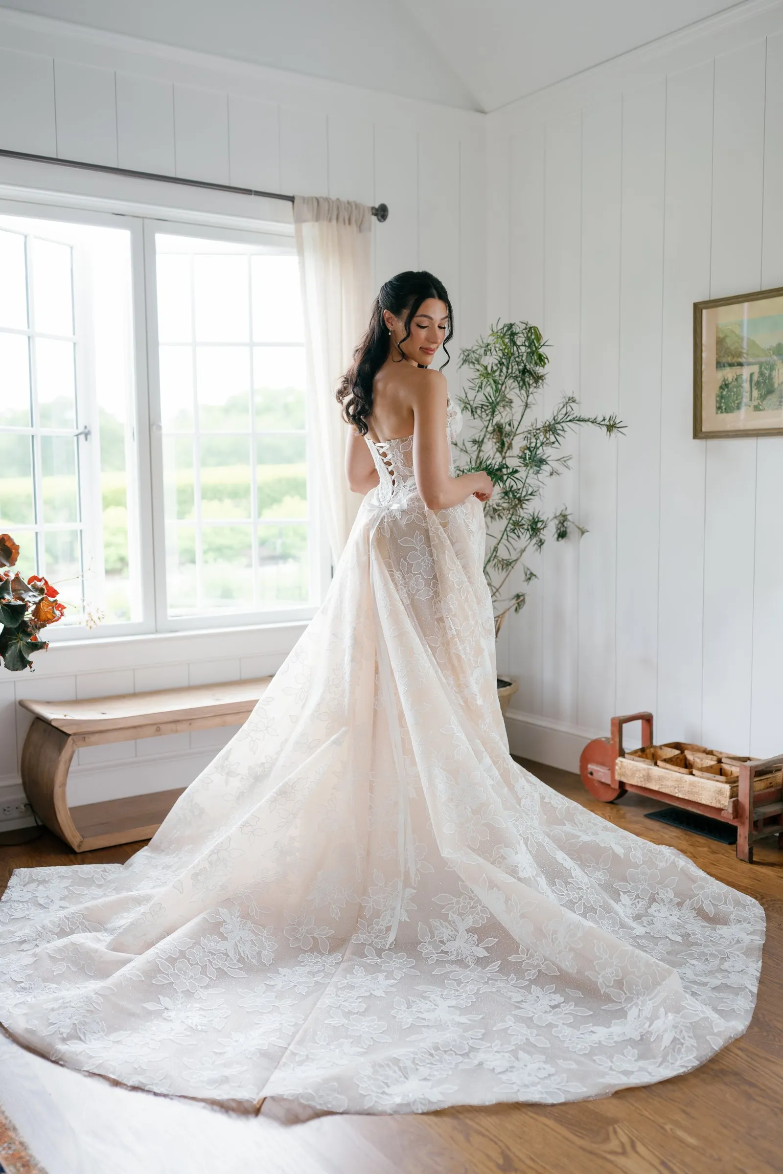 Kayla in her gown with its long train, standing by the cottage windows