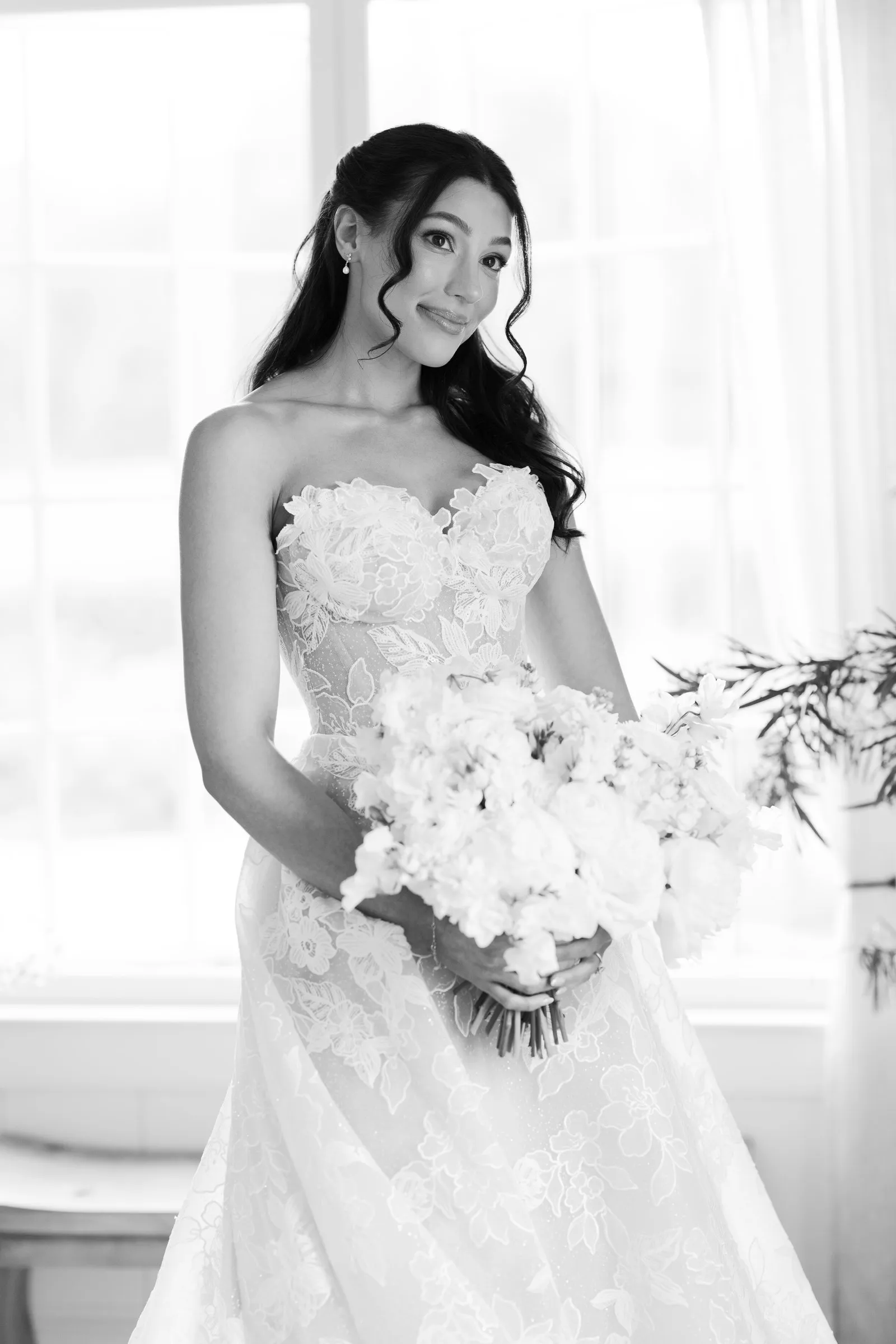 Kayla holding her white bouquet by the window, in black and white