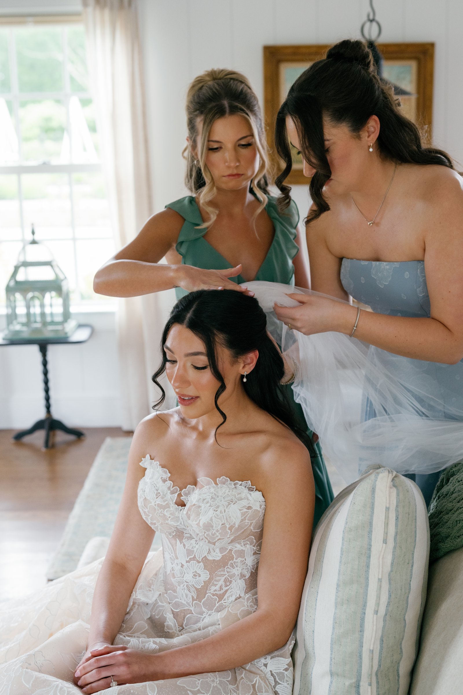 Kayla's bridesmaids setting her veil as she sits on the sofa