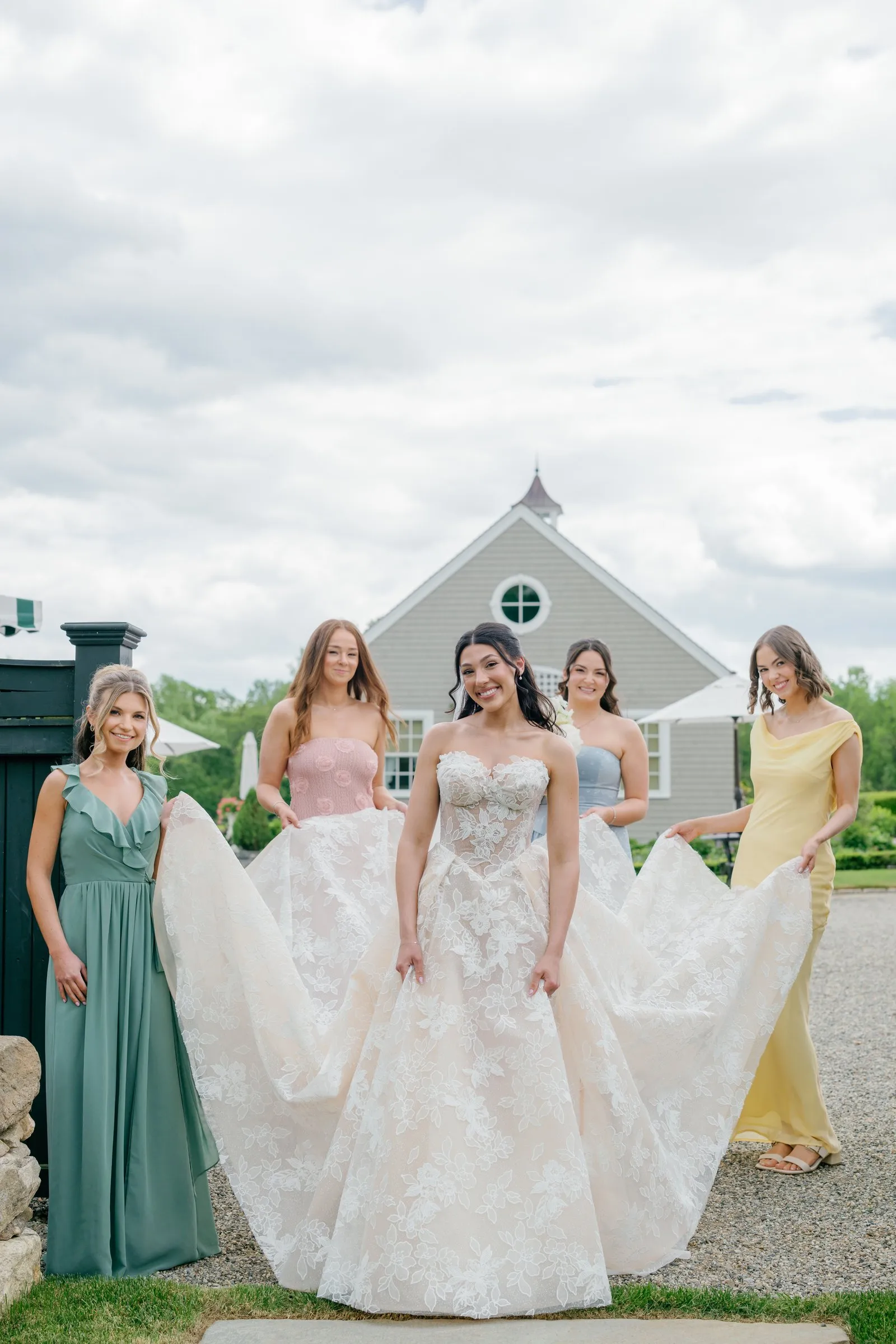 Kayla's bridesmaids carrying her train across the gravel courtyard