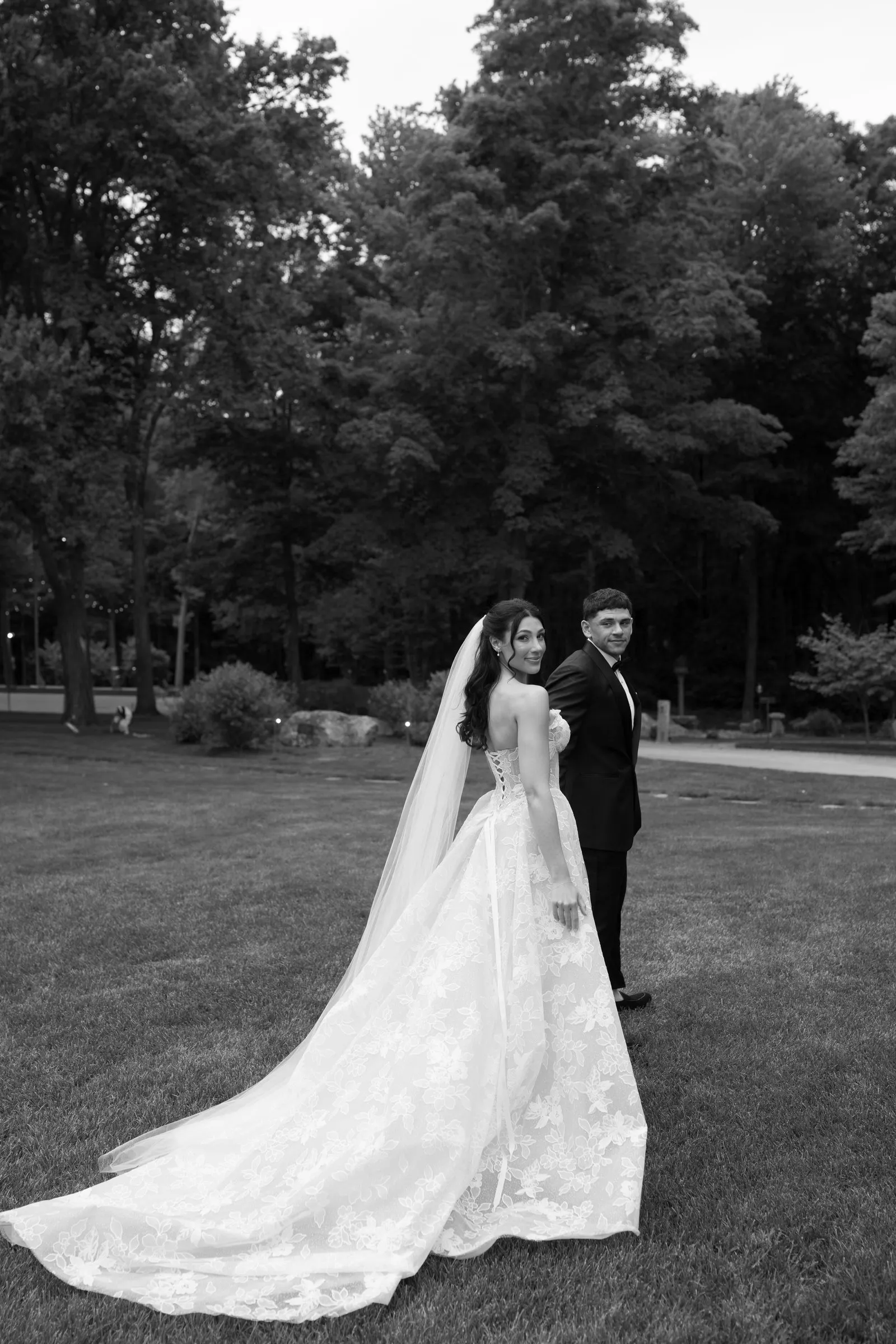 Kayla and Avery on the lawn with her veil and train spread behind her, in black and white