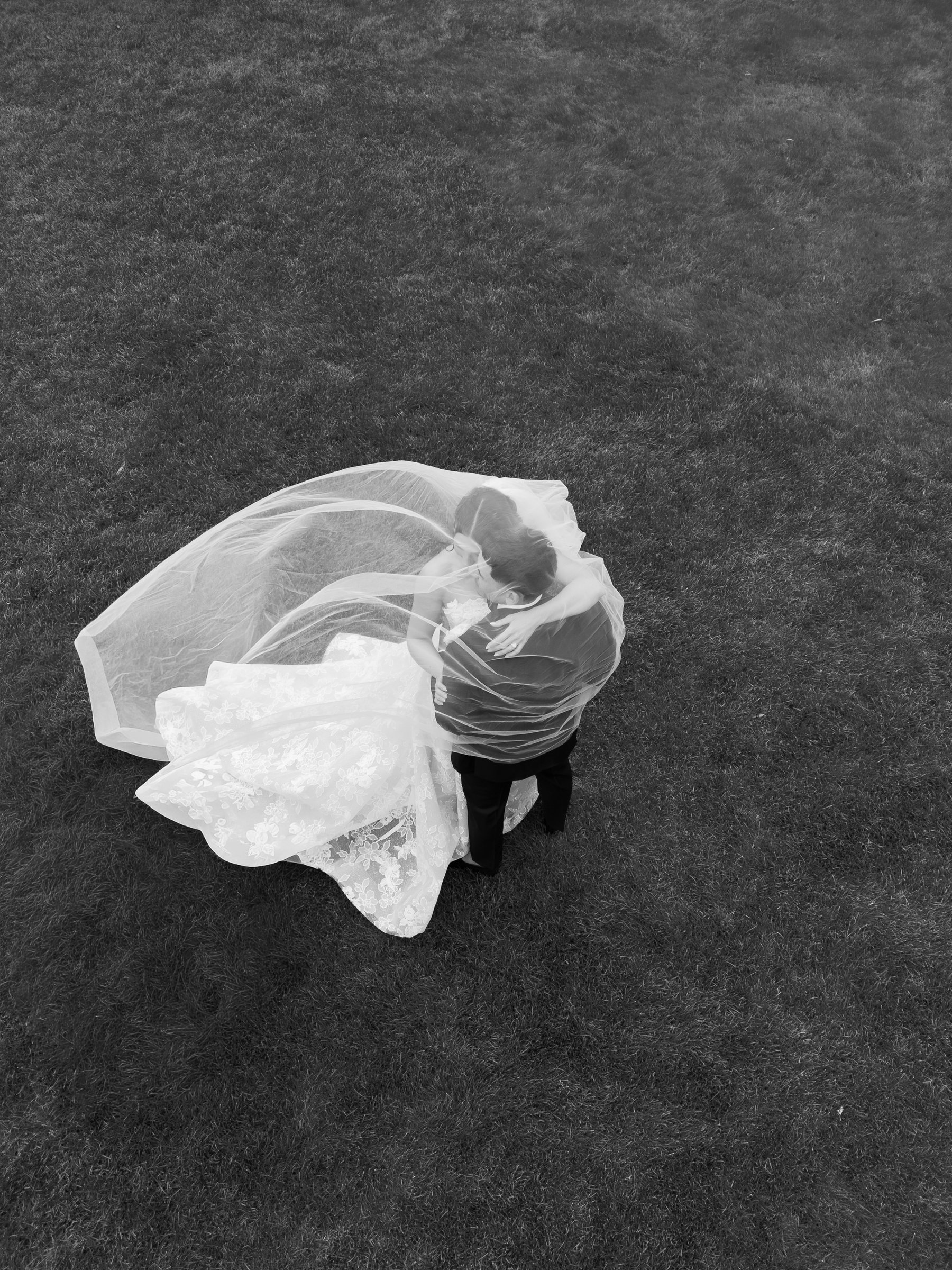 Kayla and Avery wrapped in her veil on the lawn, seen from above, in black and white