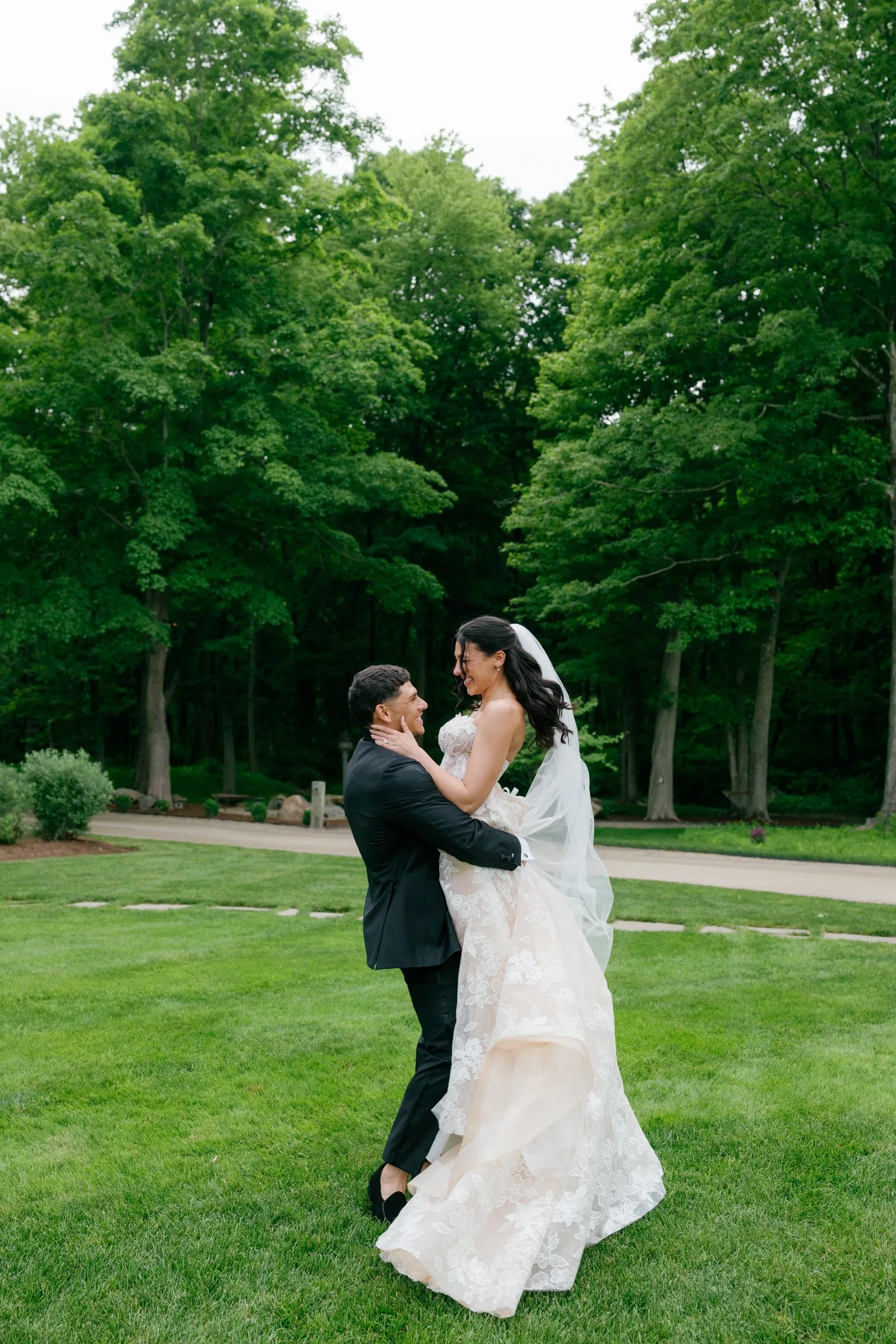 Avery lifting Kayla on the lawn with tall trees behind them