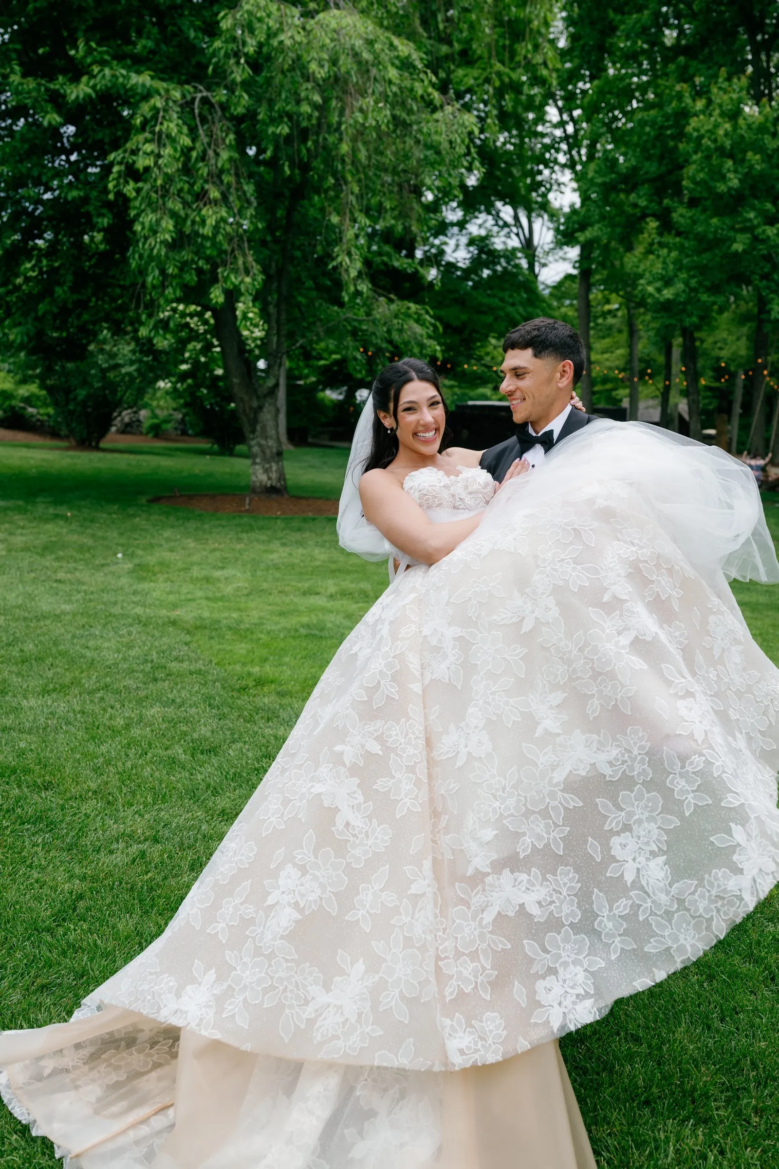 Avery carrying Kayla across the lawn, her gown spilling over his arms