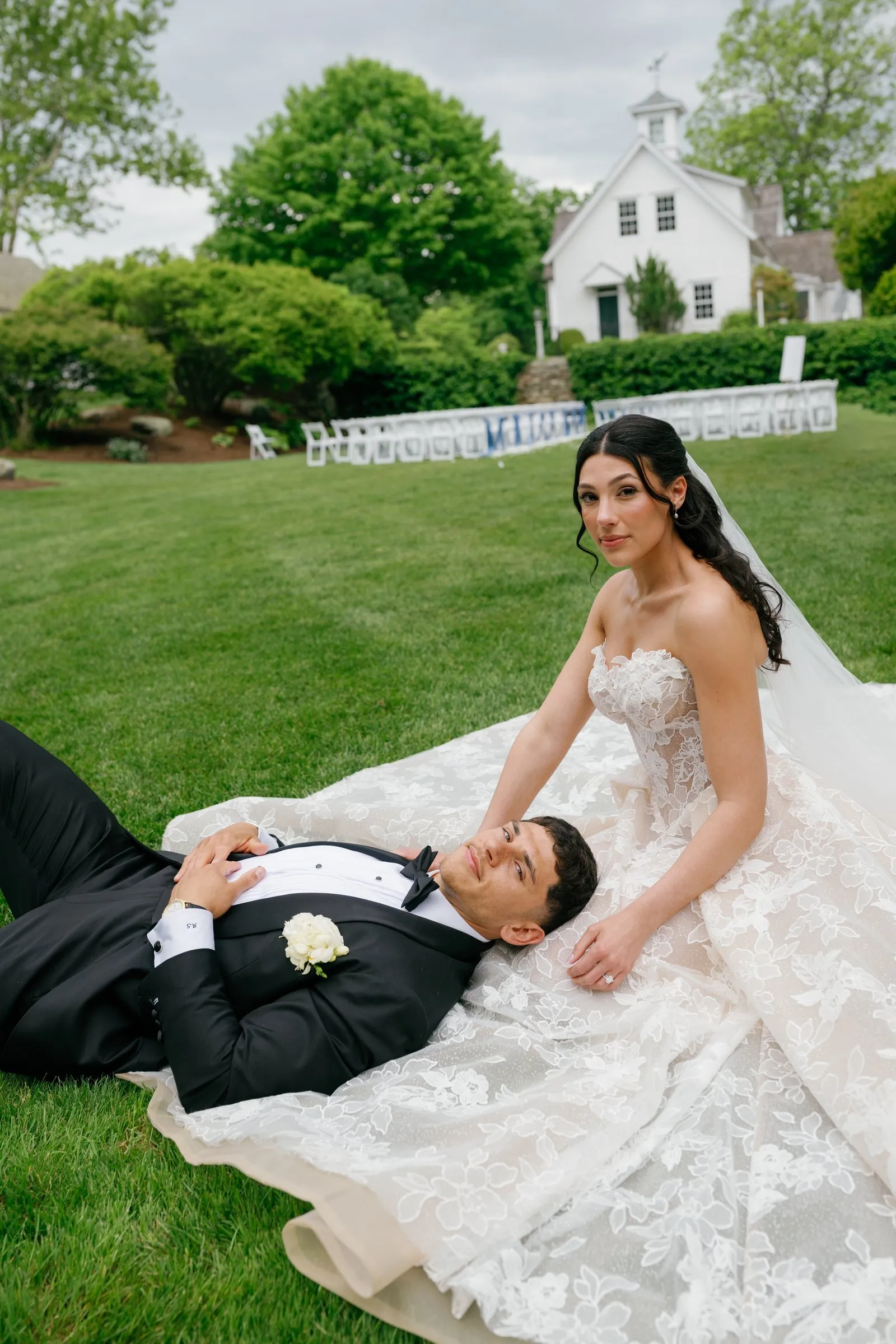 Avery lying on Kayla's gown on the lawn, the white chapel behind them