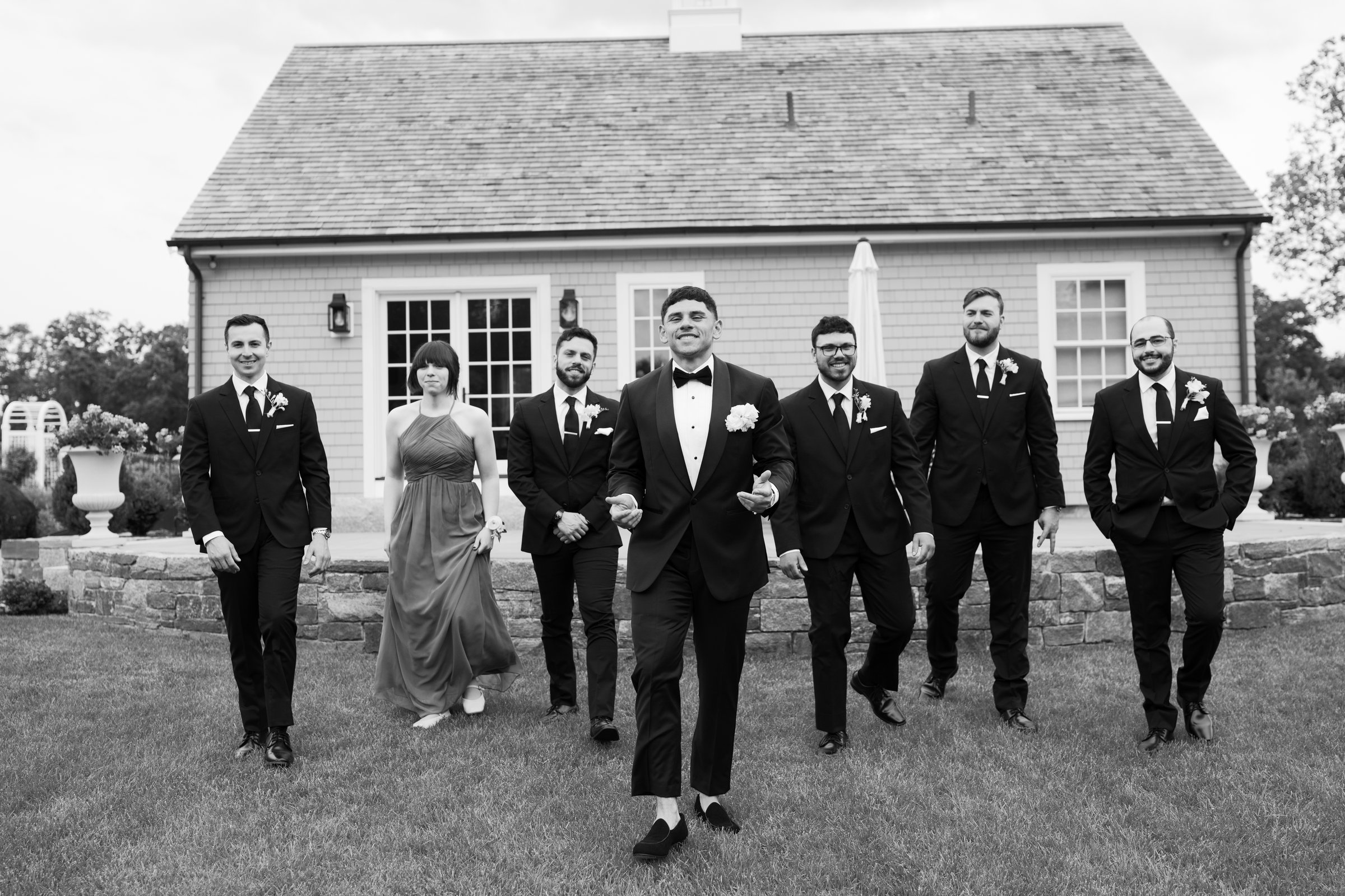 Avery and his groomsmen walking across the lawn in front of the barn, in black and white