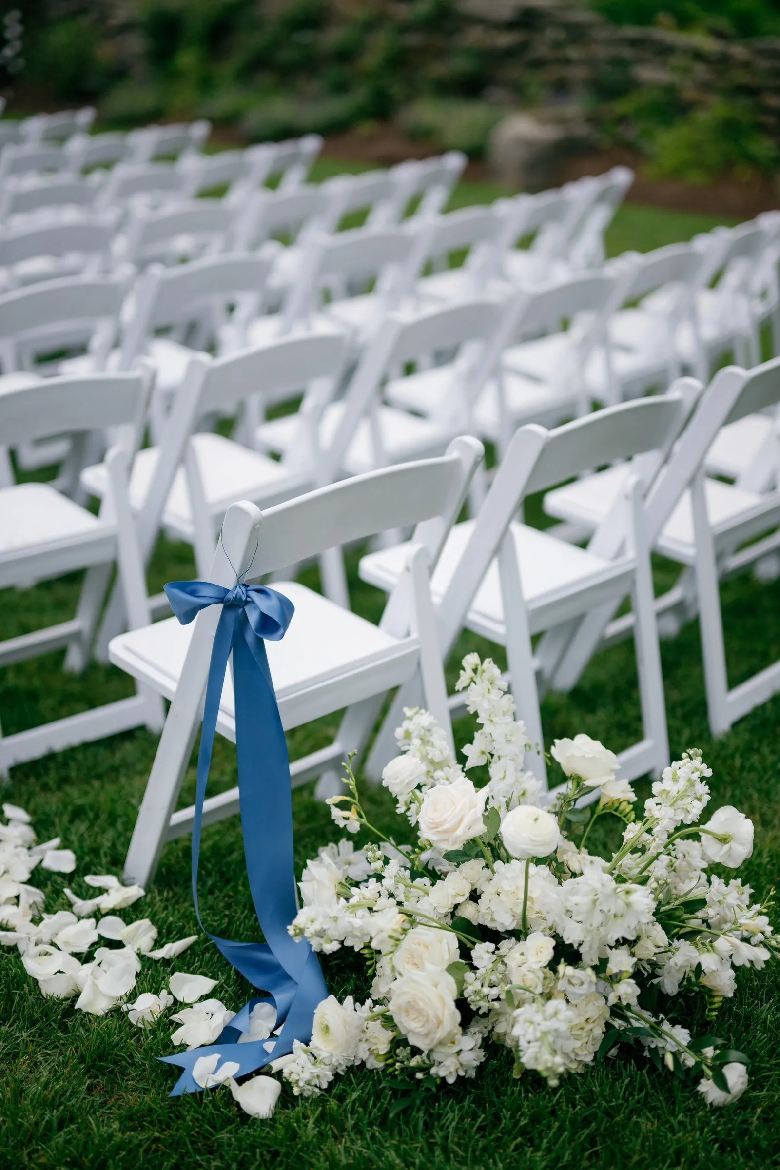White ceremony chairs with blue ribbons and white flowers along the aisle