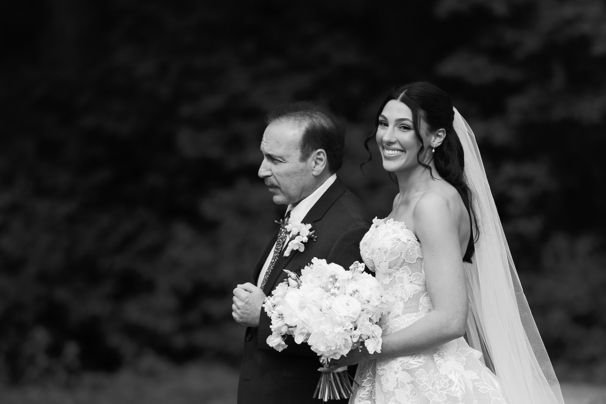 Kayla and her father smiling as they wait to walk down the aisle, in black and white
