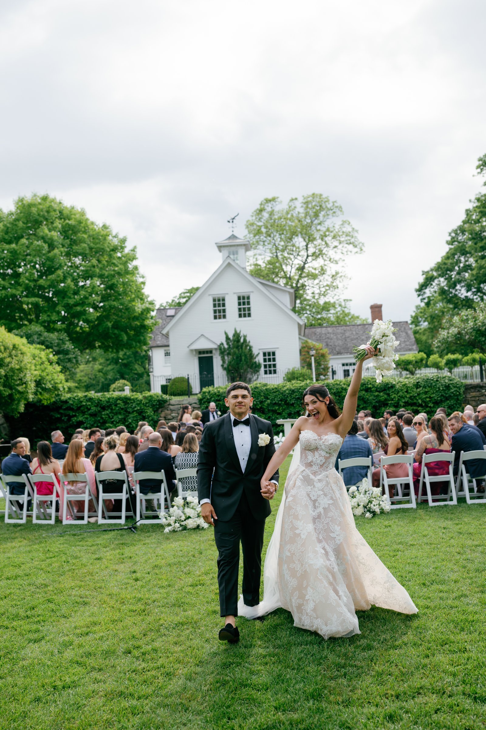 Kayla raising her bouquet as she and Avery walk back up the aisle