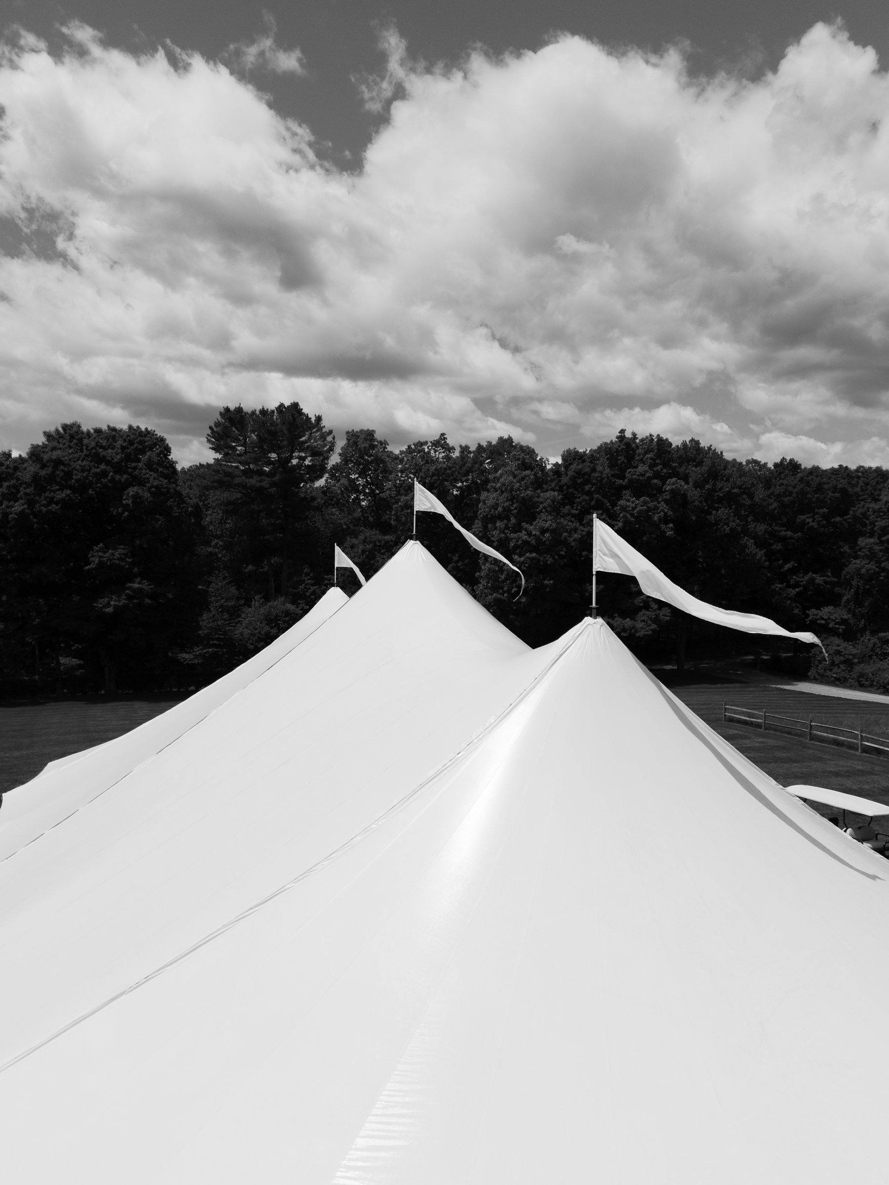 The peaks of the sailcloth tent against the clouds, in black and white