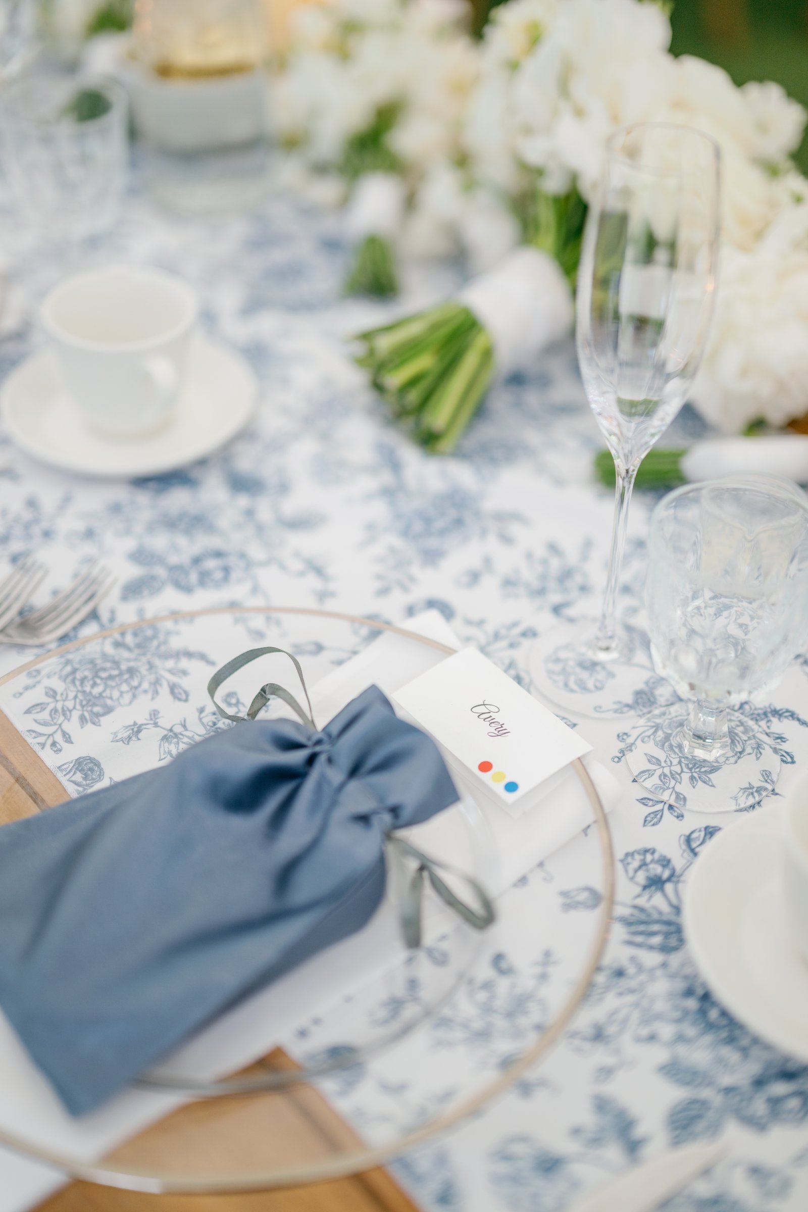 A place setting with a blue napkin tied in a bow on toile linen