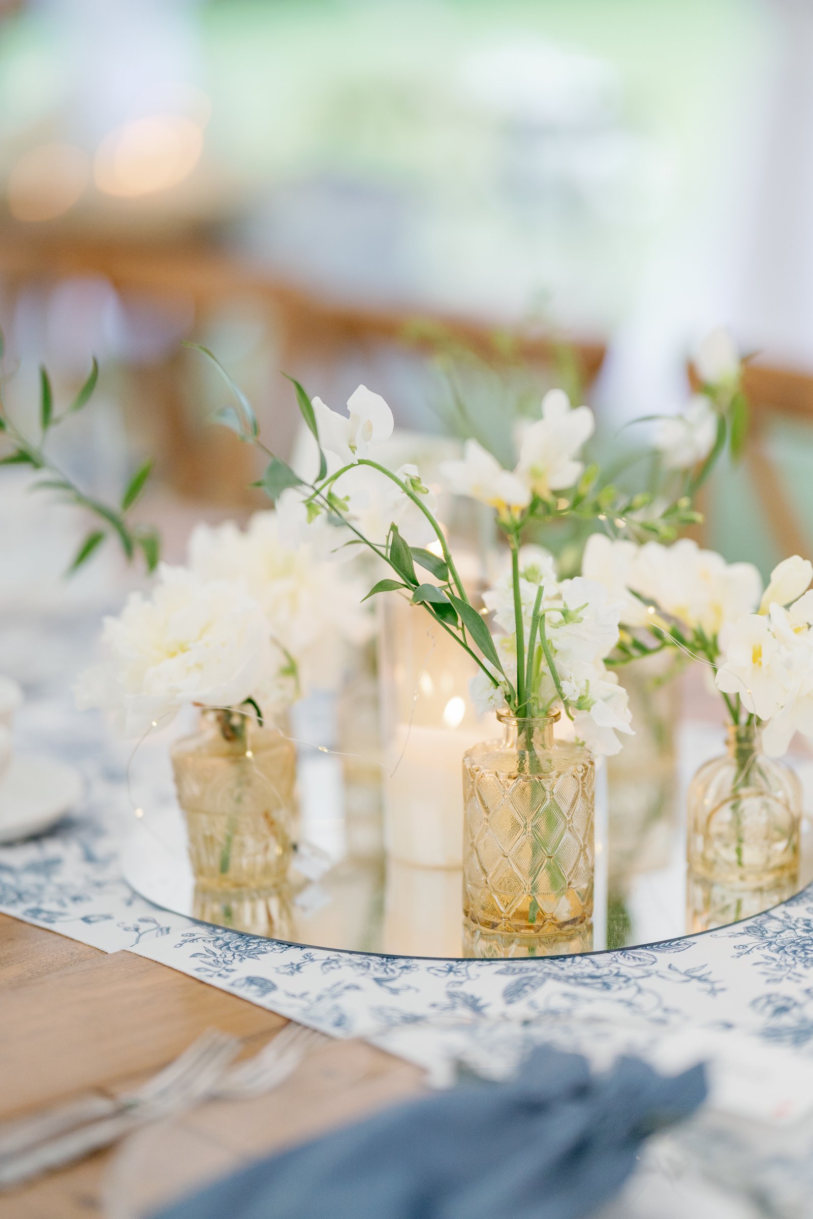 White flowers in gold vases with candles on a mirrored centrepiece