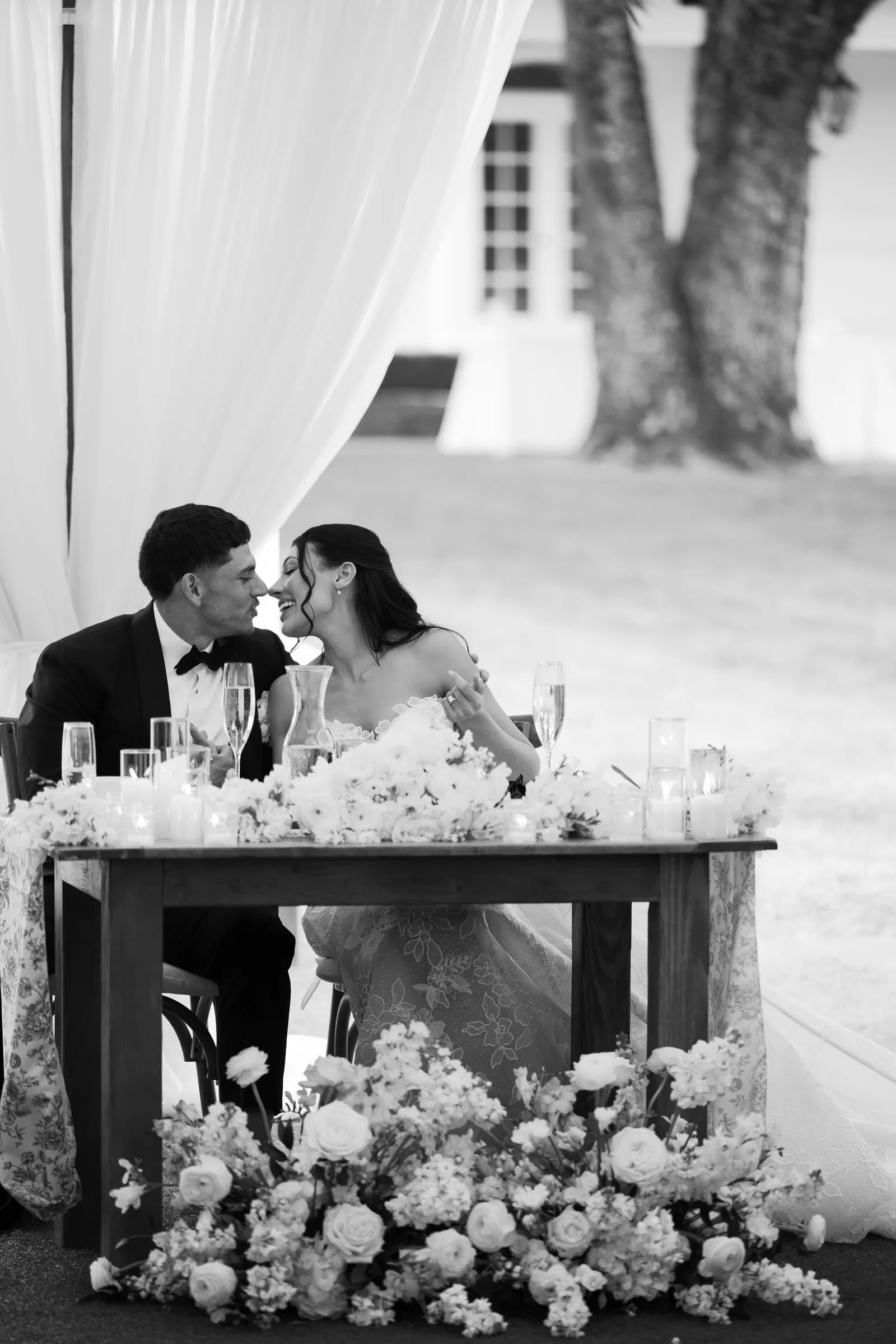 Kayla and Avery kissing at the sweetheart table, in black and white