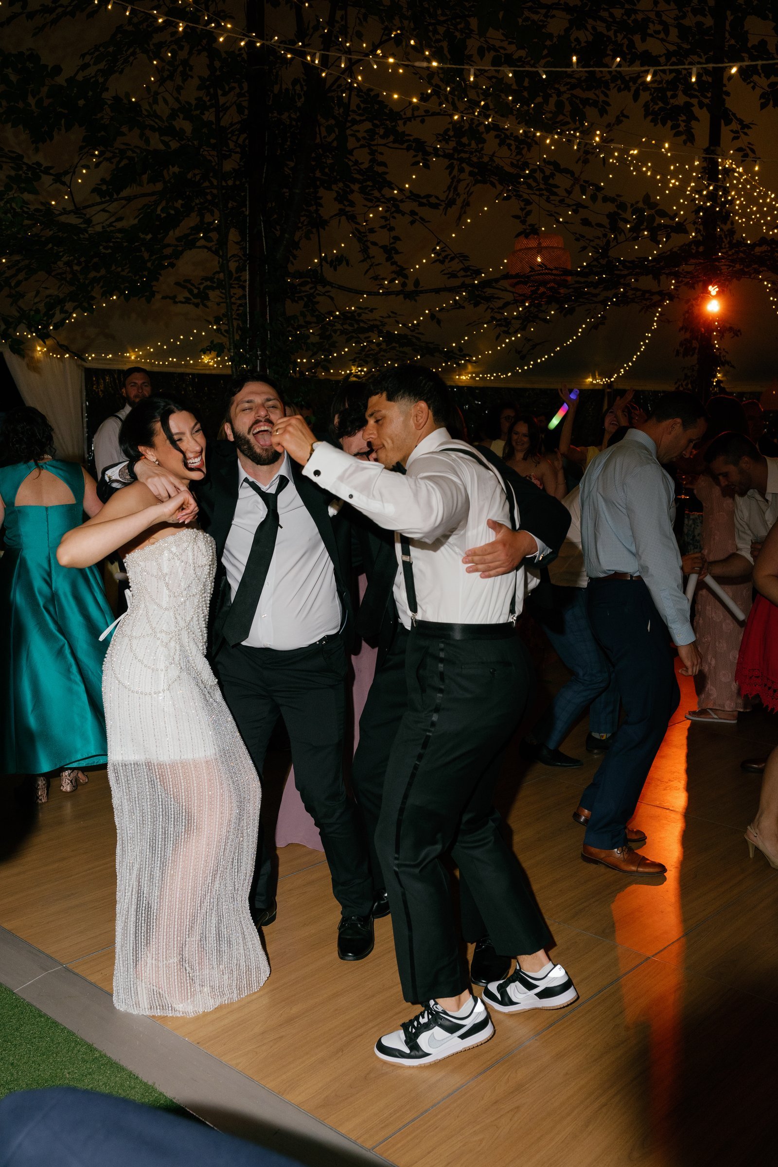 Kayla dancing with Avery and a groomsman on the dance floor under the tent lights