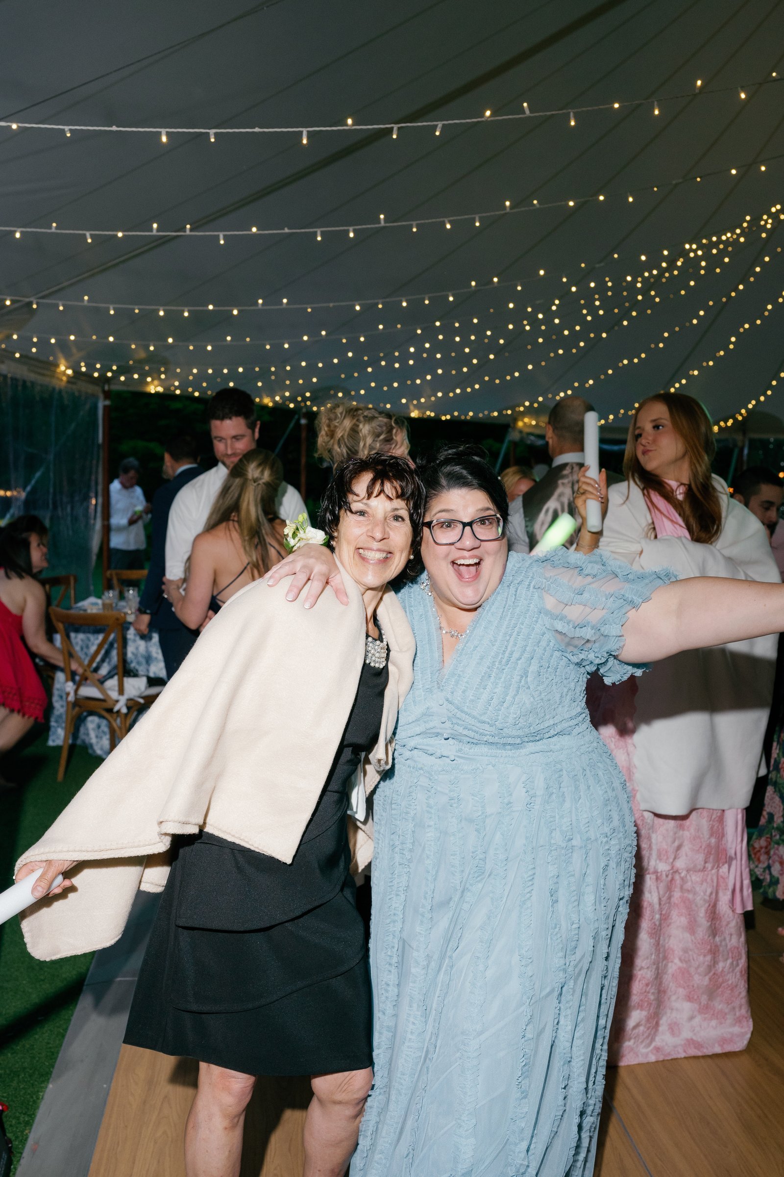 Two guests laughing and dancing together under the string lights in the tent
