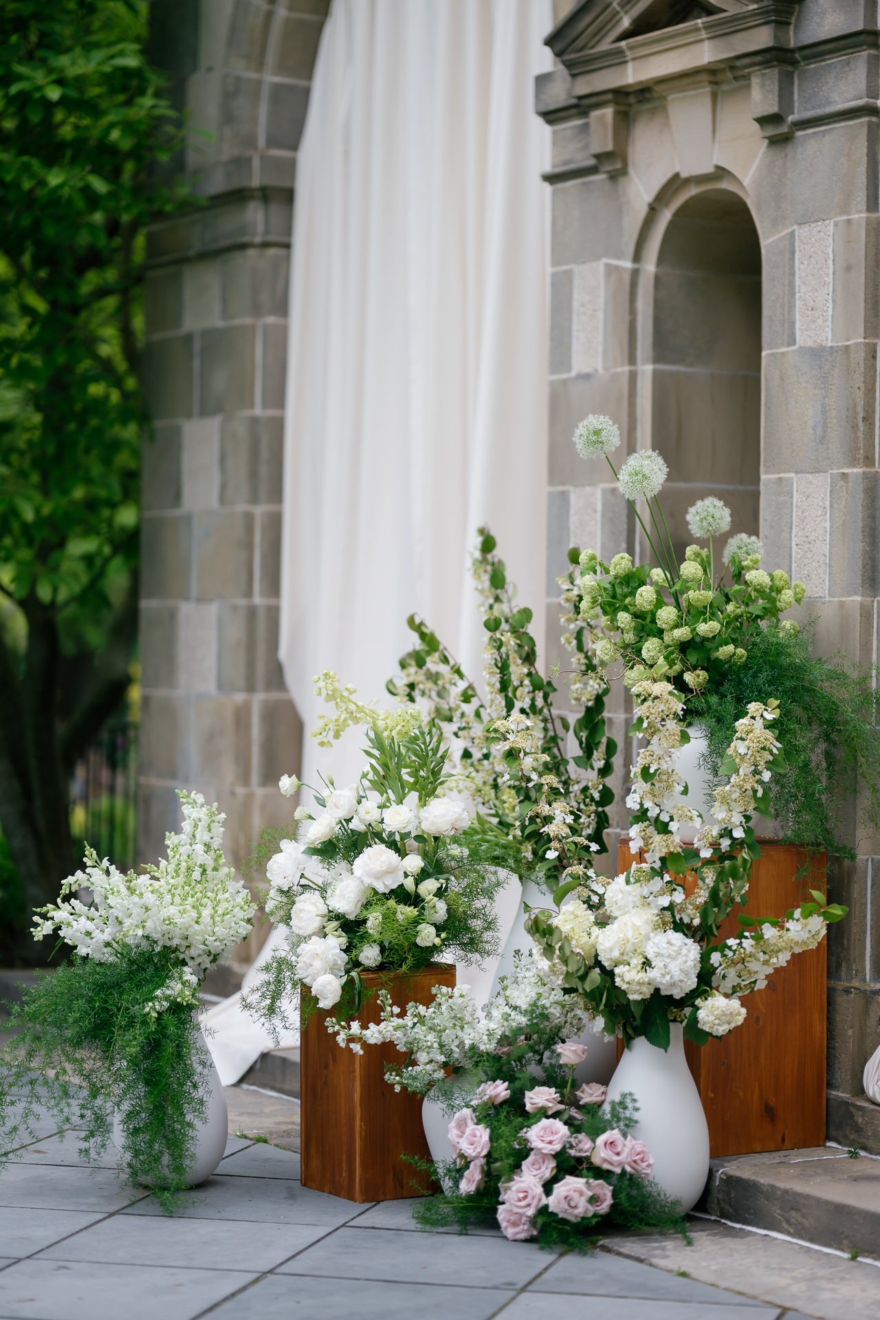 Floral urn of white and blush flowers at a stone arch. Photographed by Shukhrat Kamalov.