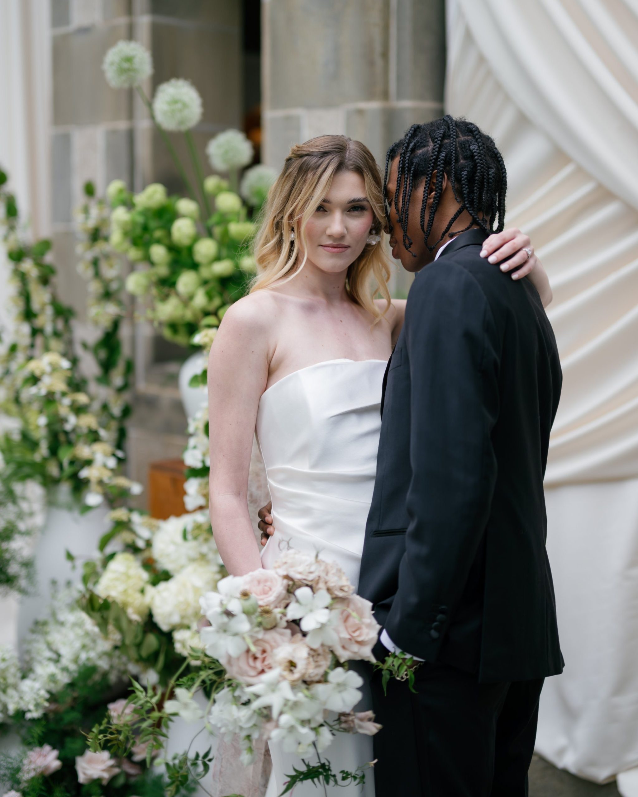 Bride and groom in black tie beside white florals and stone, Glen Manor House editorial. Photographed by Shukhrat Kamalov.
