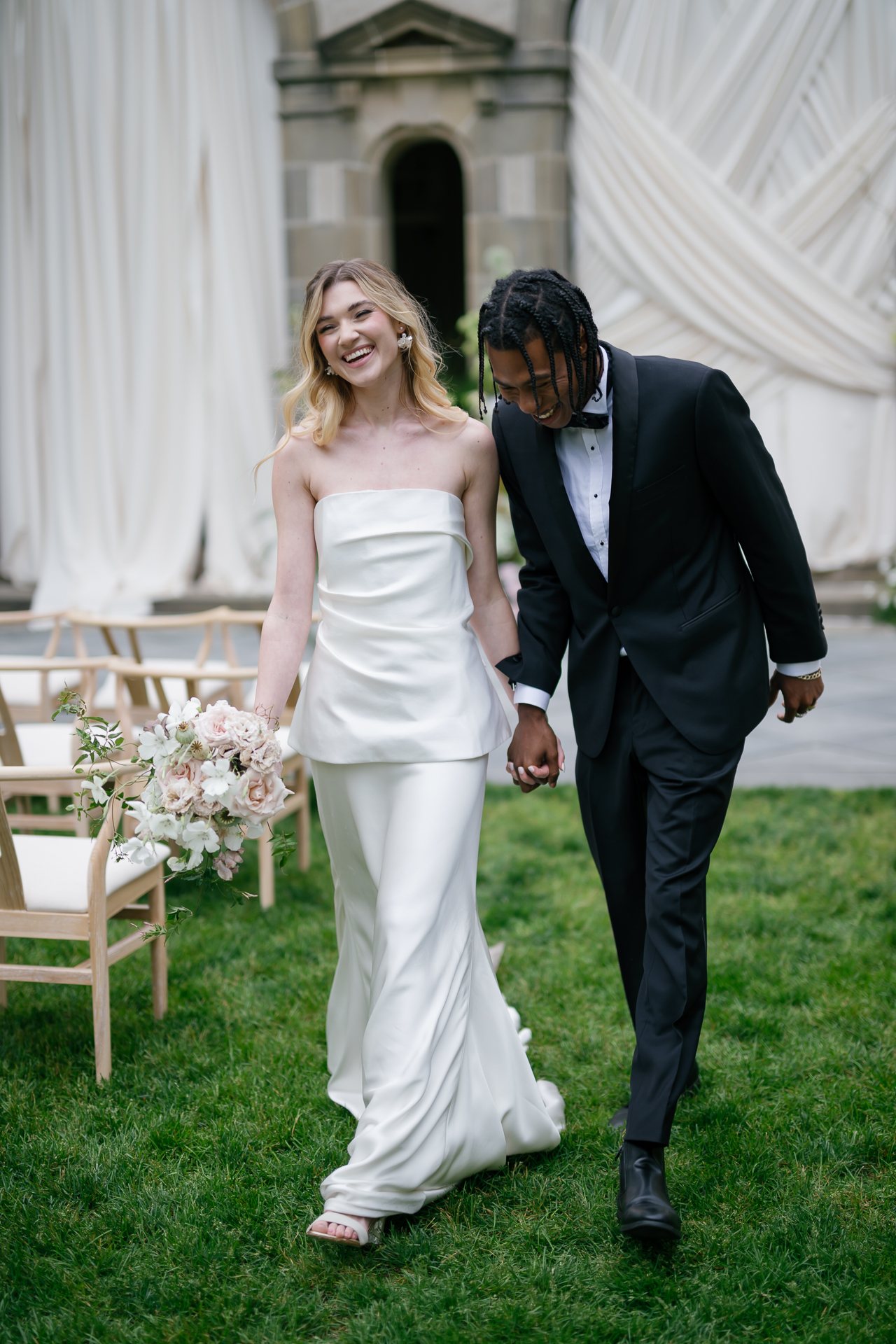 Bride and groom in black tie walking across the lawn. Photographed by Shukhrat Kamalov.