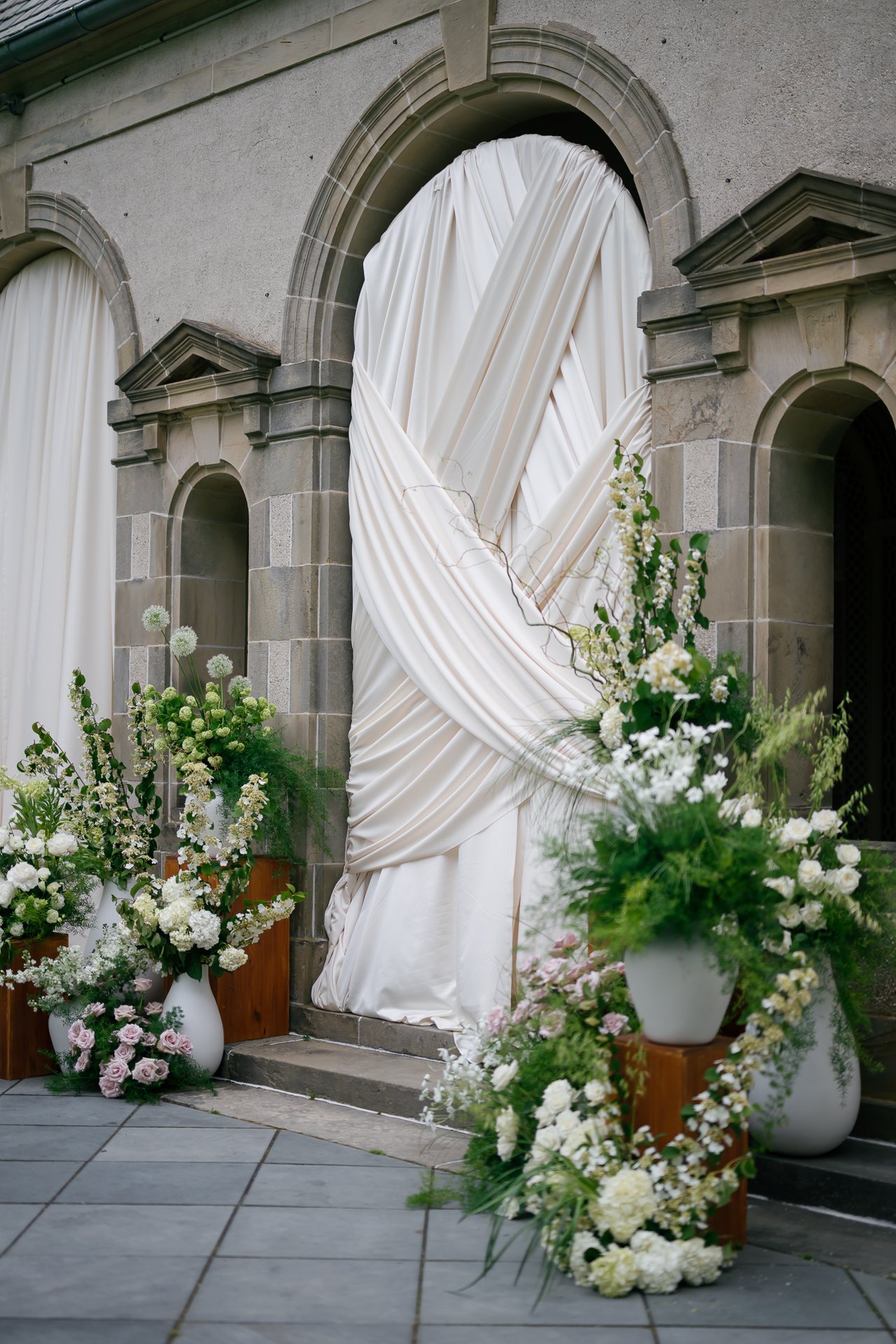 Ivory draped stone arch with tall white and green florals. Photographed by Shukhrat Kamalov.