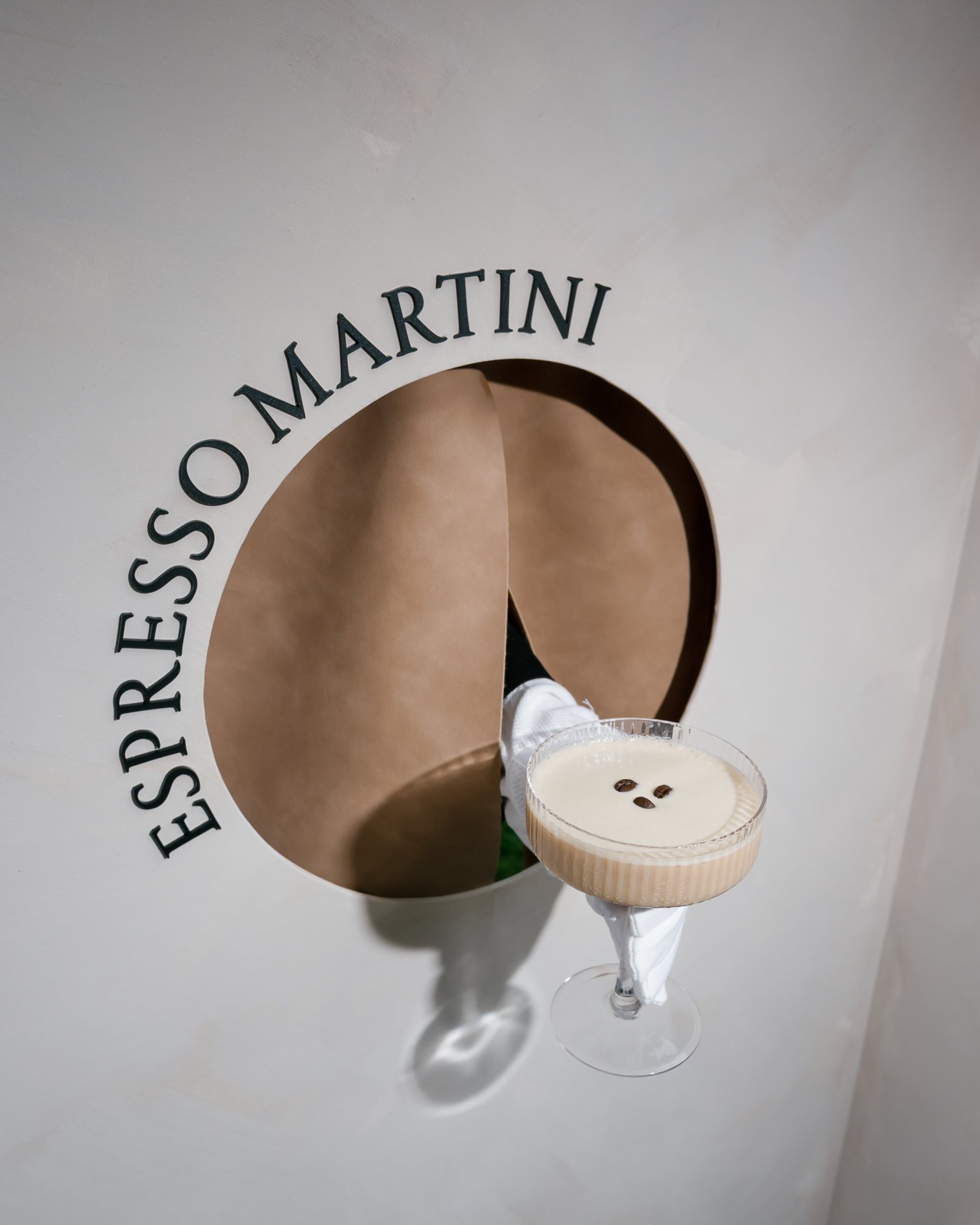 Espresso martini served through a round hatch in a white wall. Photographed by Shukhrat Kamalov.