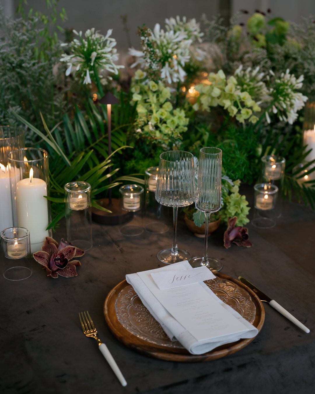 Place setting with florals and candles on a dark table. Photographed by Shukhrat Kamalov.