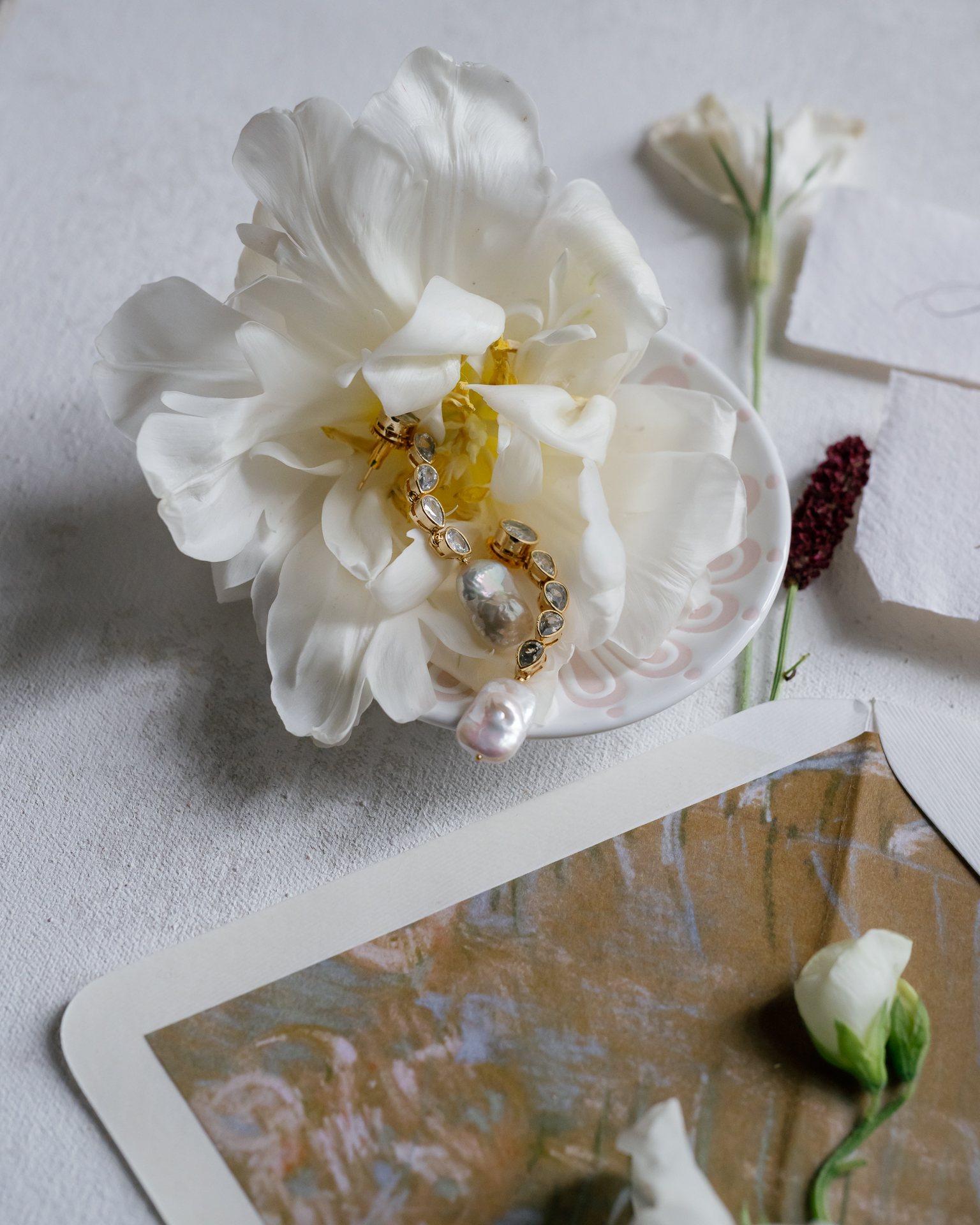 Wedding rings resting in a white peony beside the paper. Photographed by Shukhrat Kamalov.