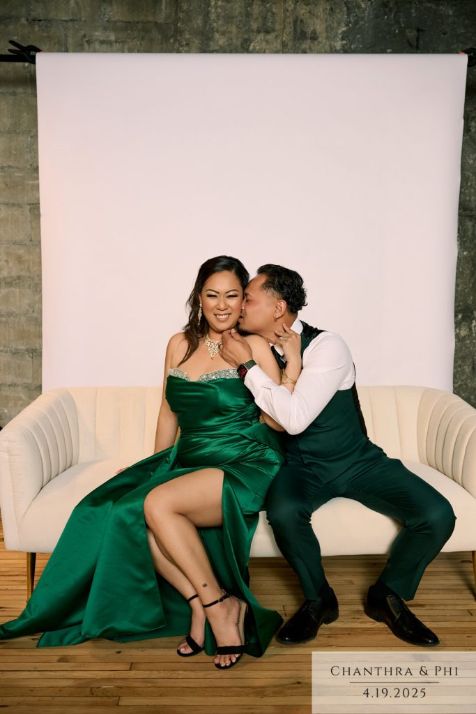 Wedding guests on the Portrait Lounge sofa, she in an emerald gown, he kisses her cheek